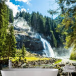 Fototapeten Wasserfall in den Bergen inmitten eines üppigen grünen Waldes.